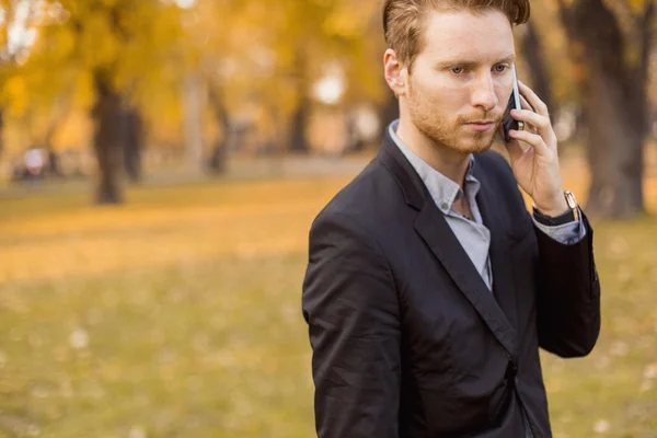 Jovem com telefone celular no parque de outono — Fotografia de Stock