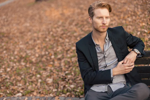 Young man at the bench in autumn park — Stock Photo, Image