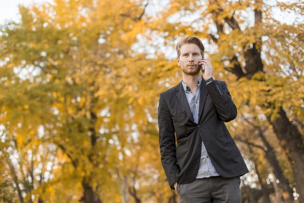 Молодой человек с мобильным телефоном в осеннем парке — стоковое фото