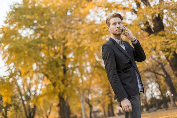 Молодой человек с мобильным телефоном в осеннем парке — стоковое фото