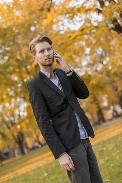 Jovem com telefone celular no parque de outono — Fotografia de Stock