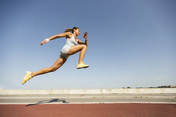 Jovem mulher tomando salto em comprimento — Fotografia de Stock