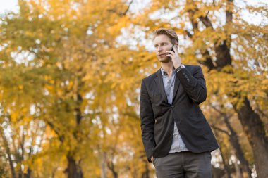 Güz parkında cep telefonu olan genç bir adam.