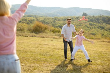 A father and his child play catch with a frisbee in a grassy field. They are laughing and having fun under sunny skies with mountains in the background on a clear autumn day.