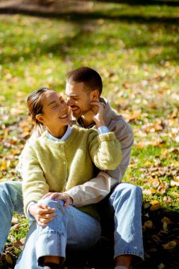 Genç çok ırklı çift, düşen yapraklarla dolu canlı bir parkta gülüşlerini ve sıcaklığını paylaşıyor. Birlikte güzel bir sonbahar gününü yakalıyorlar..