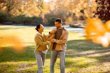 İki mutlu birey güzel bir parkta neşeli bir anı paylaşıyor, canlı sonbahar yapraklarıyla çevrili, gülümseyen ve birbirlerinin arkadaşlığından keyif alan..