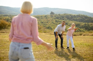 Aile üyeleri açık alanda, güneşin altında frizbi oynarken harika vakit geçiriyorlar. Neşeli atmosfer bağlarını ve ortak gülüşlerini gösteriyor..