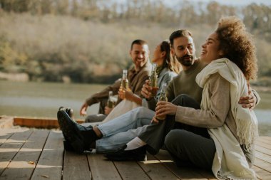 Neşeli beş arkadaşından oluşan bir grup göl kenarında dinleniyor, güneşli bir öğleden sonra içkilerini ve kahkahalarını paylaşıyor, doğayla iç içe..