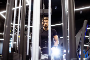 Bir adam akşamleyin Marko Loncar Spor Salonu 'nda spor aletleriyle antrenman yapıyor. Spor yaparken konsantrasyonunu gösteriyor, fitness ortamının enerjisini vurguluyor..