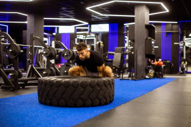 Formda bir adam yoğun bir antrenmana katılır, trendli ve iyi donanımlı bir spor salonunda büyük bir lastiği patlatır. Atmosfer enerjik ve motive edici..