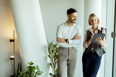 İki meslektaş, büyük pencerelerde durarak proje detaylarını bir tablette gözden geçirirken hafif bir anın keyfini çıkarıyorlar. Gülüşleri çağdaş bir ofiste olumlu bir çalışma ortamı olduğunu gösteriyor..