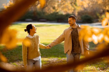 Sonbahar yapraklarıyla dolu güzel bir parkta, Koreli bir kadın ve beyaz bir adam el ele yürür, güneşli gökyüzünün altında neşeli bir gülümseme paylaşırlar..