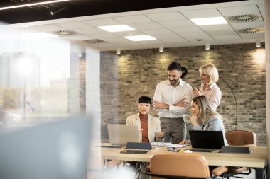 Çeşitli profesyonellerden oluşan bir grup, iyi aydınlatılmış taş duvarlı bir ofiste dizüstü bilgisayarlı bir masada fikirleri tartışarak bir toplantıya katıldı. Odaklanmış ve işbirlikçi görünüyorlar, takım çalışması sergiliyorlar..