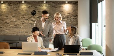 Dört profesyonelden oluşan bir grup şık ve modern bir ofiste canlı bir tartışmaya girişiyor. İki kişi dizüstü bilgisayarlı masalarda otururken, diğer ikisi ayakta fikir ve belgeleri paylaşıyor..