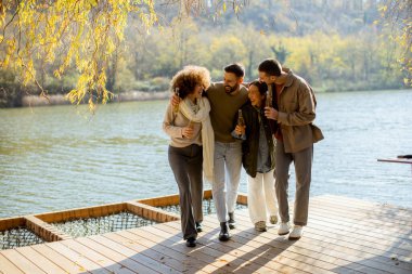 Dört arkadaş, güneşli bir sonbahar gününde gölün kıyısındaki ahşap bir rıhtımda gülerek ve içkinin tadını çıkararak yürür. Canlı yapraklar onları çevrelemiş..