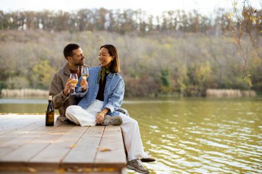 Neşeli bir çift sakin gölün kenarında oturur, güler ve kadehlerini şarap kadehleriyle kaldırır, güzel bir günde birlikte ıslanırlar..