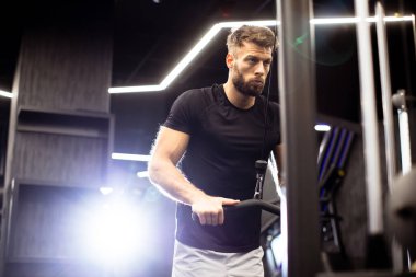 Genç adam modern bir spor salonunda çalışıyor. Akşamki güç antrenmanı sırasında forma olan bağlılığını gösteriyor. Atmosfer enerjik ve motive edici..