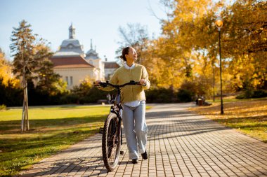 Parlak sonbahar yaprakları, bisikletle gezen Koreli bir kadının etrafını sarıyor. Huzurlu bir parkta güneşin tadını çıkarıyor..
