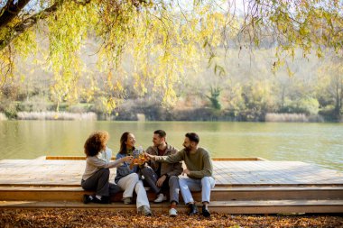 Dört arkadaş gölün kıyısındaki ahşap bir platformda oturup renkli sonbahar yaprakları ve dingin doğayla çevrili içkilerini ve kahkahalarını paylaşıyorlar..