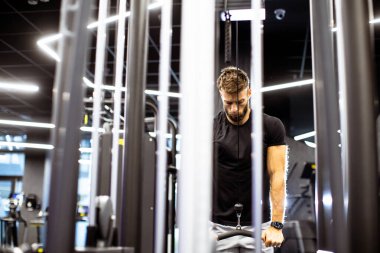 Adam modern bir spor salonunda vücut gücünü arttırmak için kablo makinelerini kullanarak sabah antrenmanına odaklanıyor. Parlak ayarı atmosfere enerji veriyor..