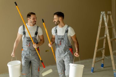 İki adam bir odanın duvarlarını seve seve boyuyor. Yanlarında merdiven olan boya ruloları ve kovalar tutuyorlar. Sıcak açık kahverengi renk uzaya hoş bir atmosfer ekler..