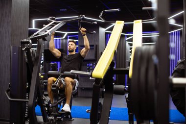 Gelişmiş ekipman ve parlak ışıklarla dolu gösterişli bir spor salonunda spor yapan bir adam kendini adamışlığını sergiliyor..