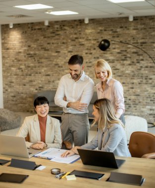 Four professionals gather in a contemporary office, sharing ideas while reviewing documents and using laptops. The atmosphere is creative and engaging, fostering teamwork and communication.