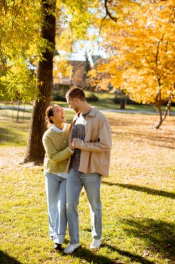 İki insan, canlı sonbahar yaprakları ve gün ışığıyla el ele yürürken mutlu bir anı paylaşıyor..