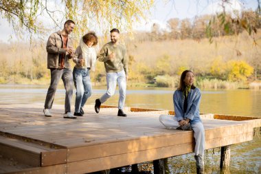 Bir grup arkadaş, sakin bir gölün kıyısındaki ahşap bir rıhtımda toplanır, güler ve altın sonbahar güneşinin altında birbirlerine eşlik ederler..