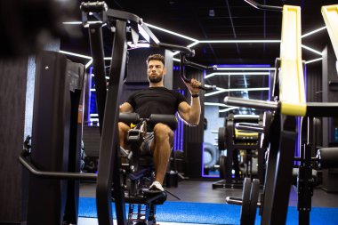 Çağdaş bir jimnastik salonunda bir kişi son sürat çekme makinesi kullanıyor. Parlak ışıklar ve modern ekipmanlar odaklanmış bir çalışma için davetkar bir atmosfer yaratır..