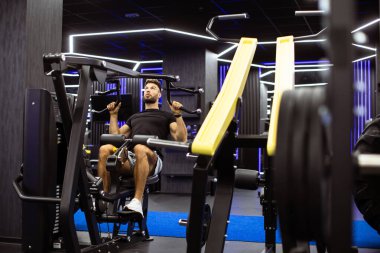 Bir adam şık bir spor salonunda bir çekme makinesini kullanırken antrenmanına odaklanır. Parlak ışıklar ekipmanı vurgular, egzersiz için enerjik bir atmosfer yaratır..
