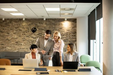 Dört profesyonel şık bir ofiste konferans masasının etrafında toplanıyor. Fikirleri tartışıyorlar ve ellerinde bir tablet ve dizüstü bilgisayarlarla belgeleri gözden geçiriyorlar..