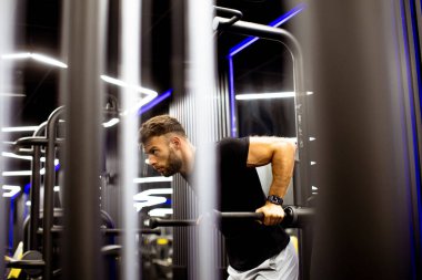 Kendini işine adamış bir adam, şık bir spor salonunda, gece boyunca odaklanarak ve güçlü bir şekilde daldırır. Etrafı parlak ekipmanlarla çevrilidir..