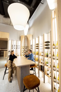 İki kişi şık bir şarap barında şişelerle canlı sohbete girişiyor. Sıcak ortam mükemmel bir zemin oluşturur..