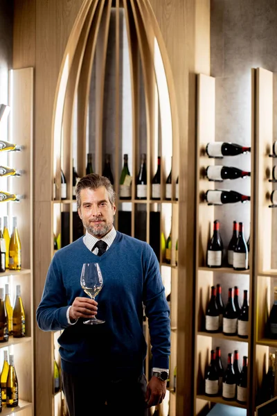 Şarap mahzeninde elinde büyük bir şarap kadehi tutan bir adam var. Şişeler ahşap raflarda sergilenir. Çevre, atmosferin tadını çıkaran adama odaklanmış durumda..