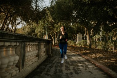 Bir kadın Malta 'da ağaçlarla çevrili bir yolda koşuyor. Güneş gökyüzünün altında, egzersiz için doğal bir ortam yaratıyor. Odaklanmış görünüyor ve anın tadını çıkarıyor..