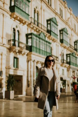 Malta 'da tarihi bir bölgede bir kadın yürüyor. O, büyük yeşil pencereli binaların yanından güvenle geçer. Güneş sahneyi aydınlatıyor ve canlı bir atmosfer yaratıyor..