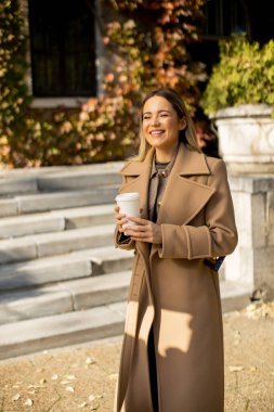 Bir kadın binanın dışındaki basamaklarda duruyor. O, sonbahar yapraklarıyla çevriliyken bir kahve fincanı tutar ve gülümser. O anın tadını çıkarırken güneş onun üzerinde parlıyor..