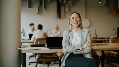 Neşeli bir iş kadını şık bir ofiste oturmuş, iş arkadaşları yakınlardaki masalarda bir tartışmayla meşgulken, keyifli bir anın tadını çıkarıyor..