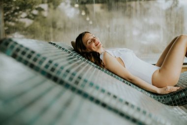 Bir kadın havuz kenarında uzanırken, güneşlenirken ve dinlenirken huzurlu bir andan zevk alır. Huzurlu atmosfer gülümsemesini arttırır..