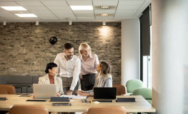 Modern bir odada dört kişi bir toplantıya katılıyor. Onlar büyük bir masada otururken fikirleri paylaşıyor ve iş tartışıyorlar. Taştan bir duvar, ayarı daha da güçlendirir..