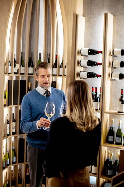 Adam ve kadın bir şarap mahzeninin içinde duruyor. Büyük şarap kadehleri tutuyorlar ve sohbetten hoşlanıyor gibiler. Arkalarındaki raflar çeşitli şarap şişeleriyle dolu..