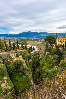 Bu pitoresk sahnede, Ronda sersemletici yeşil uçurumlarını ve dolambaçlı vadilerini gözler önüne seriyor, yumuşak bulutlu gökyüzünün altında doğanın güzelliğini gözler önüne seriyor..