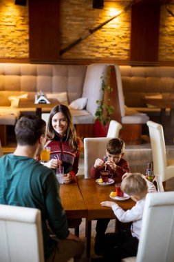 Hoş bir kafede, bir aile içeceklerin sıcaklığını paylaşır rahatlar ve bağlanır, sıcak bir atmosferde neşeli anılar yaratır..