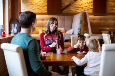 Sıcak, davetkar bir kafe ortamında bir aile kahkahalarını, içkilerini yudumluyor ve rahat bir atmosferde birlikte güzel anılar yaratıyor..