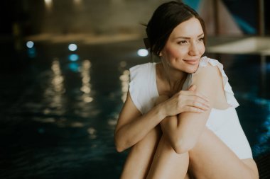 Bir kadın, serin bir spa ortamında huzur ve rahatlığı kucaklayarak, nefes kesici bir havuzun kenarında zarif bir şekilde oturur..