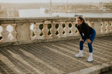 Bir kadın Malta 'da bir rıhtım kenarında egzersiz rutinine ara verir. Gün batımında ve idmandan sonra biraz soluklanıyor..