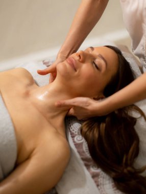 Bir kadın masaj masasında yatarken bir terapist bir sağlık merkezinde boynu ve omuzları üzerinde çalışıyor. Ortam sakin ve rahatlık ve bakım sağlamaya odaklı..