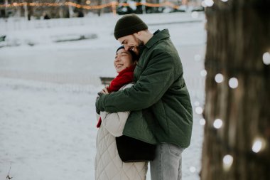 Koreli bir kadın ve beyaz bir adam karlı bir parkta birbirlerine içtenlikle gülümsüyorlar. Işıklar ve kış manzarası etraflarını sarmışken birbirlerine yakın dururlar. Kar zemini kaplıyor ve yakınlardaki ağaçlar.