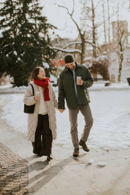 Koreli bir kadın ve beyaz bir adam karla kaplı bir parkta el ele yürüyorlar. İkisi de bardak tutuyor ve birlikte kış gününün tadını çıkarıyor gibi görünüyorlar..